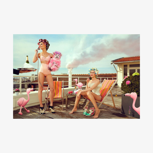 Two women in swimsuits with pink flamingos on a deck.