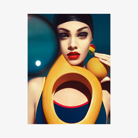 Woman in a colorful swimsuit with a yellow object in front of her face, holding a rainbow lollipop.