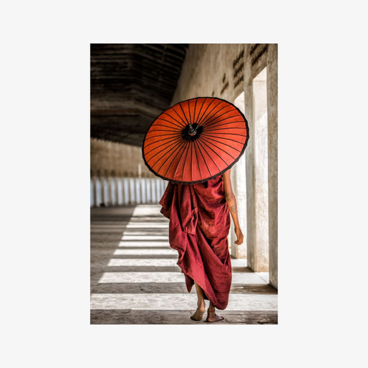 Person in red robes holding a red umbrella in a temple setting