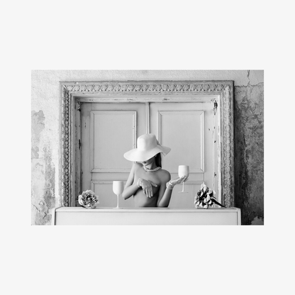 Black and white photo of a person in a hat with candles and flowers in front of a large mirror.