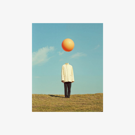 Person in a yellow coat standing on grass with an orange balloon above their head against a blue sky.