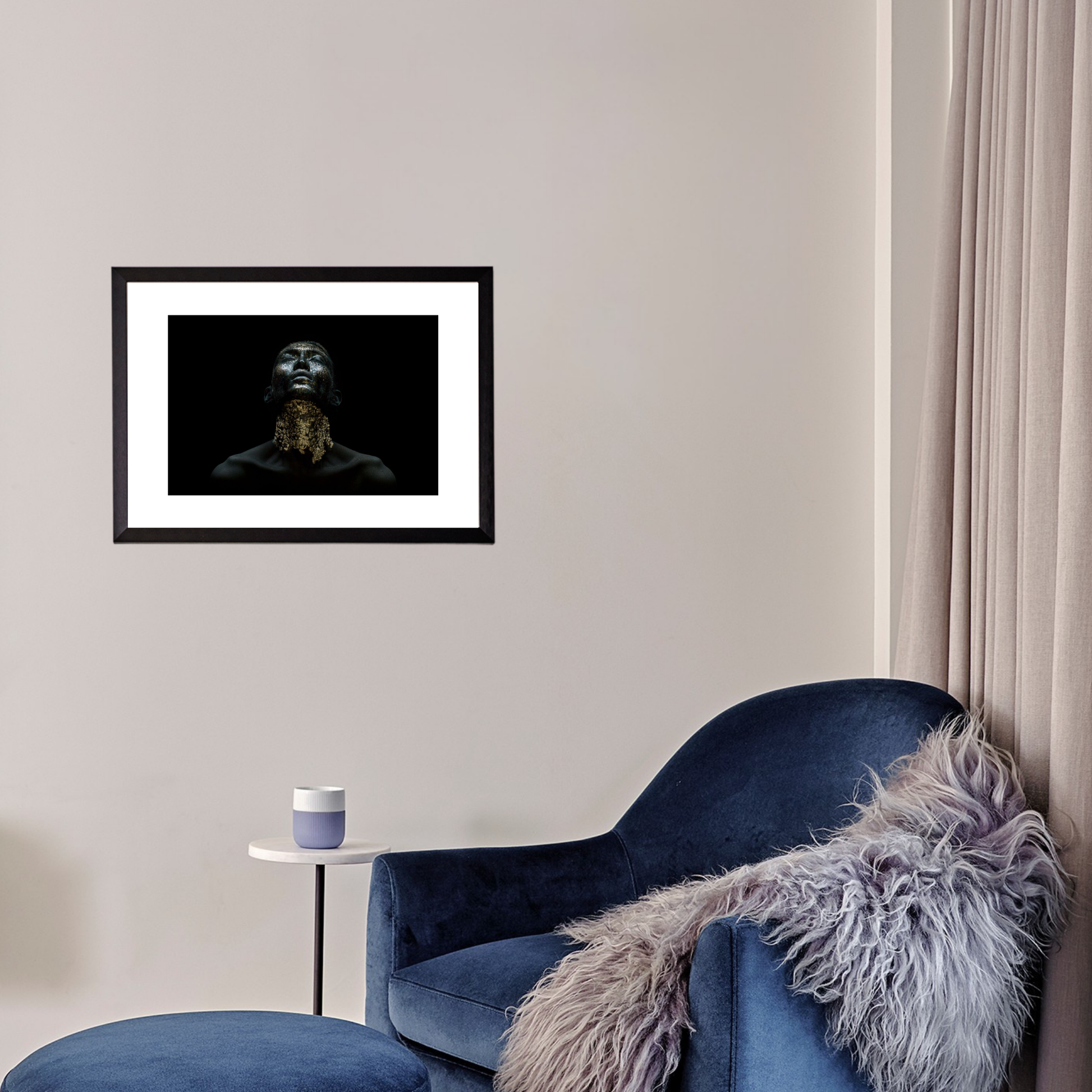 Framed artwork on a wall above a blue armchair with a fur throw.