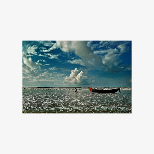 Boat on a beach with a person nearby under a blue sky with clouds.