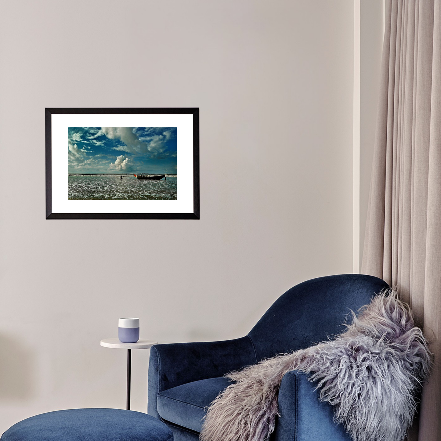 Framed artwork of a beach scene above a blue armchair with a fluffy throw.