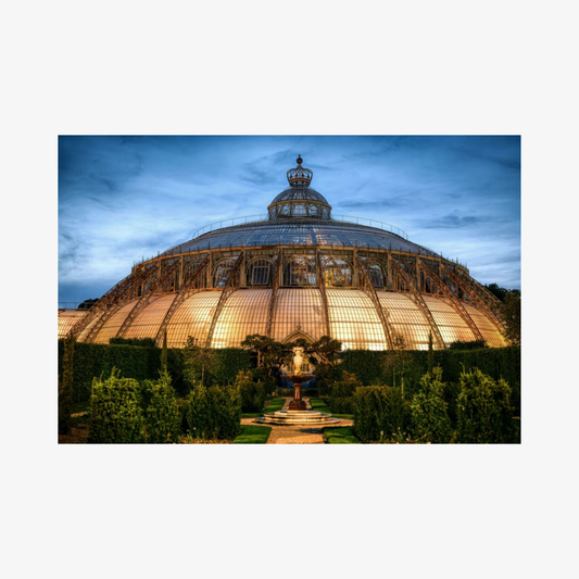 Large glass dome structure with a statue in a garden at dusk.