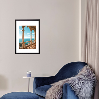 Framed artwork of a balcony overlooking the sea on a wall above a blue armchair with a fur throw.