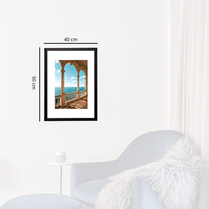 Framed artwork of a balcony with ocean view on a white wall above a white chair.
