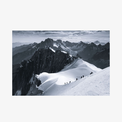 Black and white photograph of a mountain landscape with snow-covered peaks and climbers on a ridge.