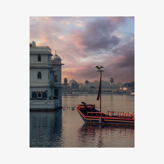 Boat on a lake with a building and colorful sky in the background