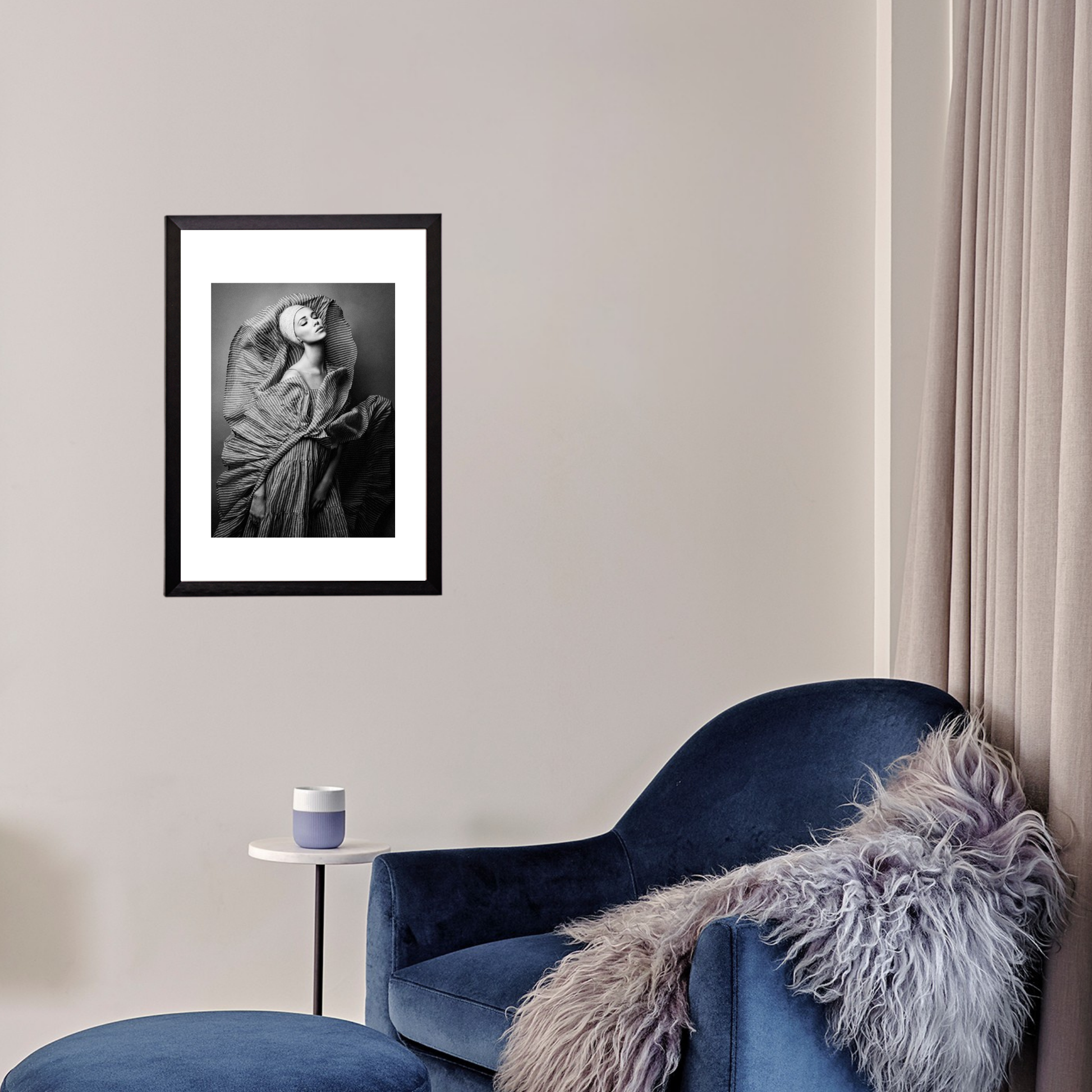 Framed artwork on a wall above a blue armchair with a fur throw.