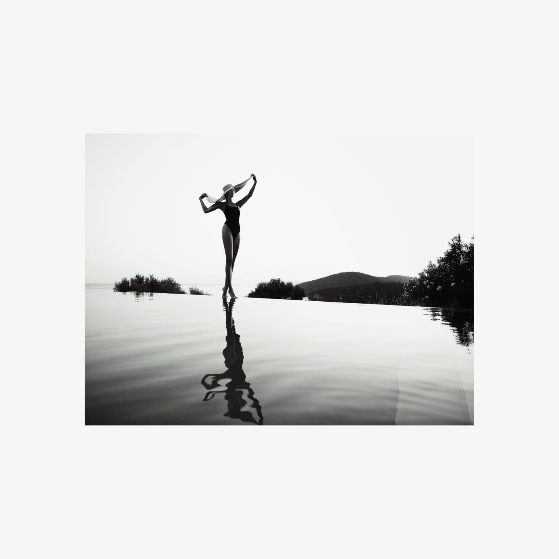 Black and white silhouette of a person standing on a lake with mountains in the background