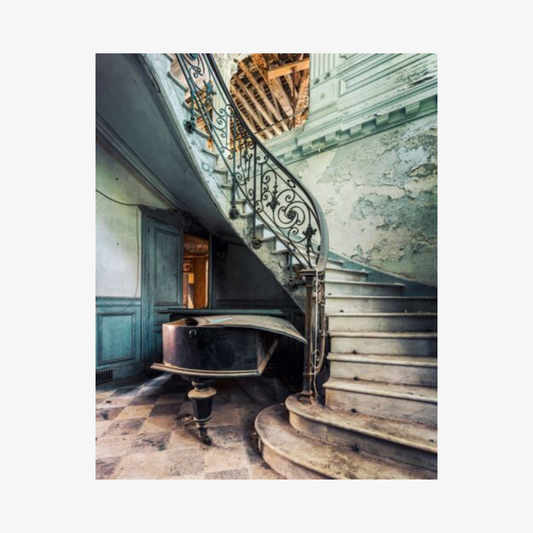 Vintage grand piano in a room with ornate staircase and peeling paint
