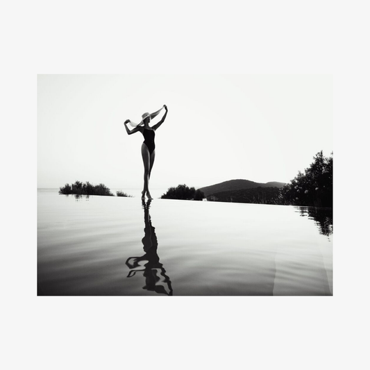 Silhouette of a person standing on a reflective lake with mountains in the background