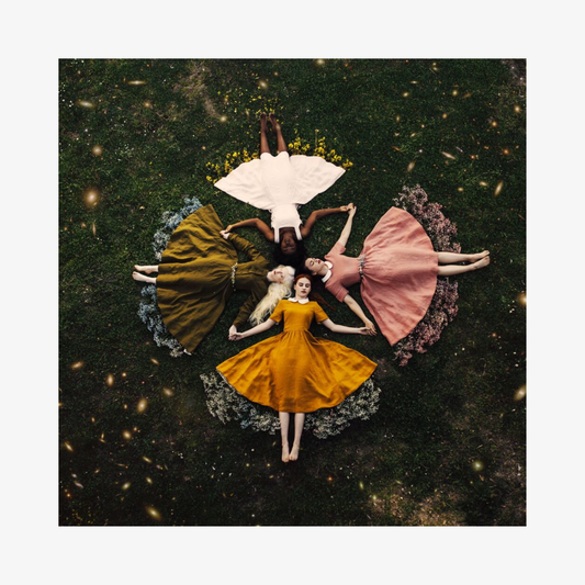 Five women in colorful dresses lying on a grassy field with a starry night sky above.