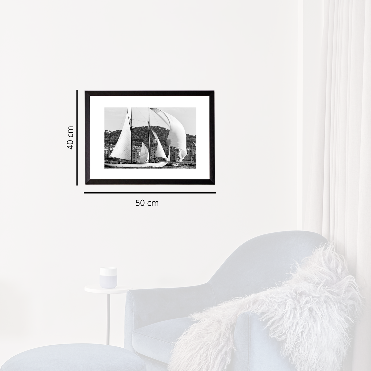 Framed black and white photograph of sailboats on a wall next to a white armchair.