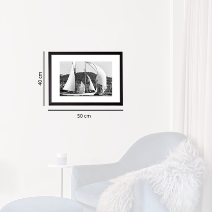 Framed black and white photograph of sailboats on a wall next to a white armchair.