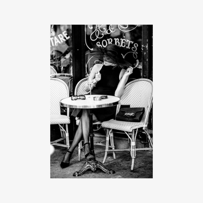 Woman sitting at a cafe table with a black bag in a black and white photo.