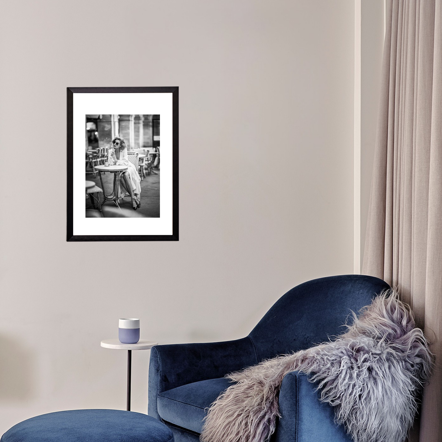 Framed black and white artwork on a wall above a blue armchair with a fur throw.