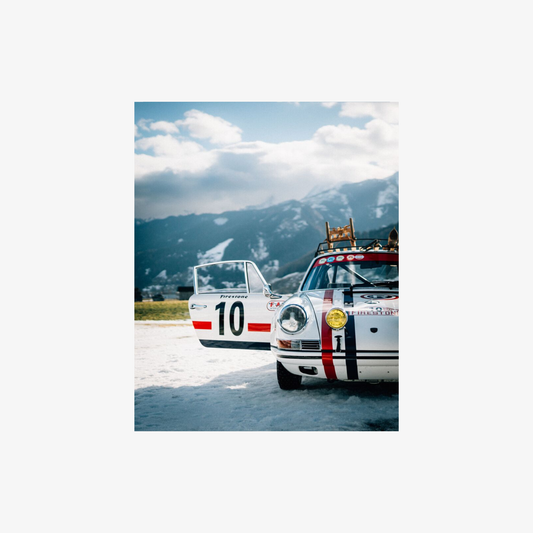 Two vintage racing cars on a track with mountains in the background