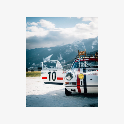 Two vintage racing cars on a track with mountains in the background